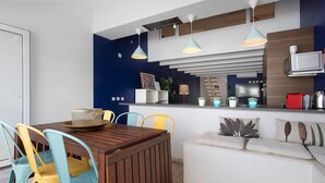 Eine moderne Küche mit Essbereich, einem Holztisch, bunten Stühlen und Pendelleuchten.