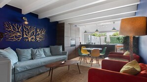 Ein modernes Wohnzimmer mit einer Couch, einem Couchtisch und Sesseln, ein Essbereich mit Tisch und Stühlen sowie eine Küche mit Schränken und Geräten.