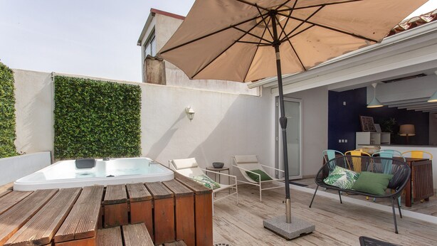 Eine Außenpatio mit Whirlpool, Holzliegen, einem Tisch, einer Hängematte und einem großen Sonnenschirm.