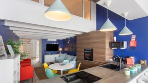 Eine moderne Küche mit einer zentralen Kochinsel, ein Essbereich mit rundem Tisch und ein Wohnbereich mit Sofa und Sesseln.