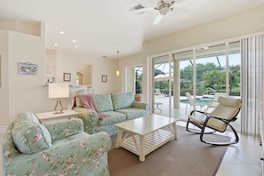 A living room with a sofa, a coffee table, a rocking chair, a lamp, and a view of the outside. - Naples Vineyards Living | Private Pool + Spa (Naples)