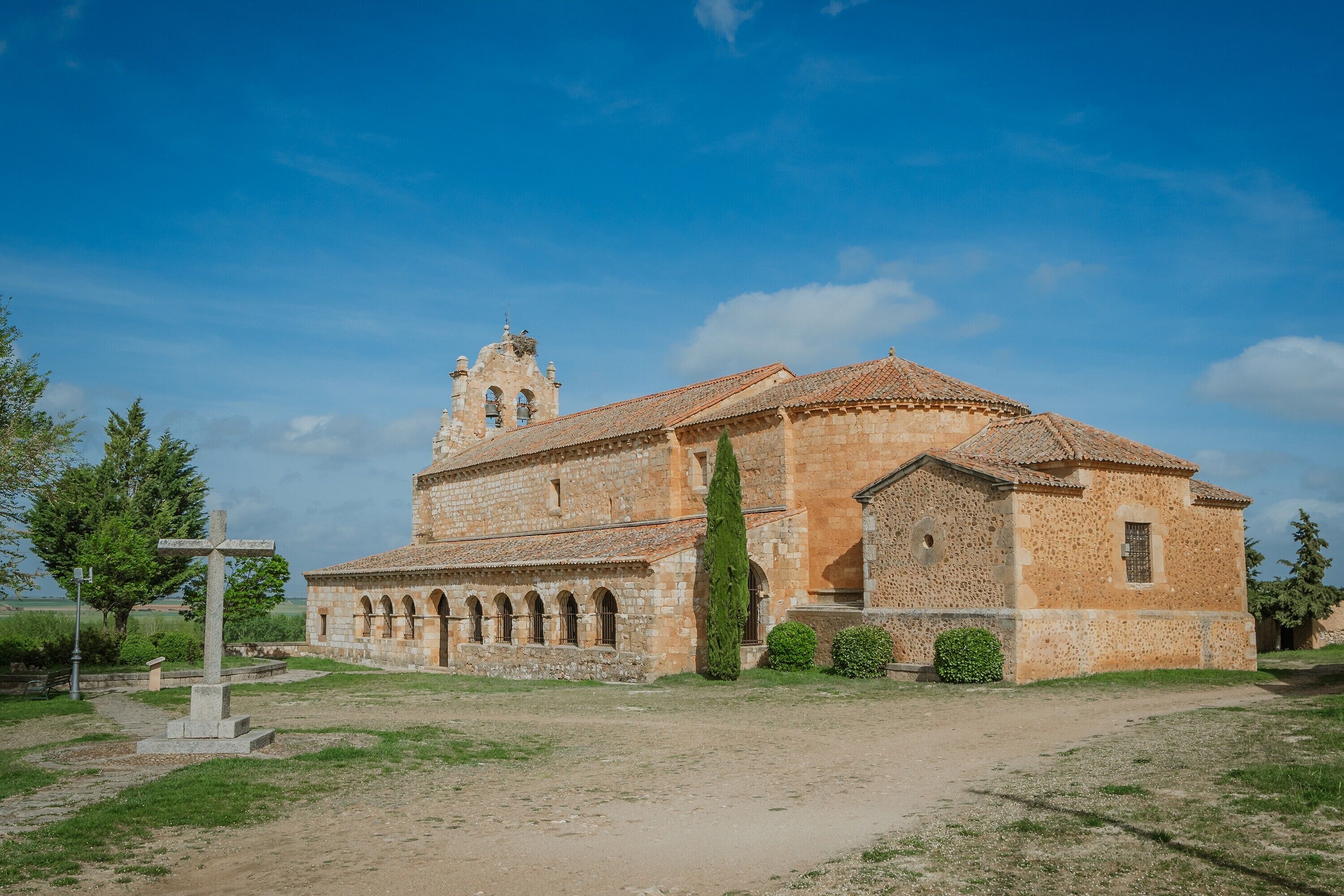 A historic stone building with a bell tower, arched windows, and a cross in the foreground.