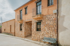 Un edificio de paredes de piedra, balcones y una banca.