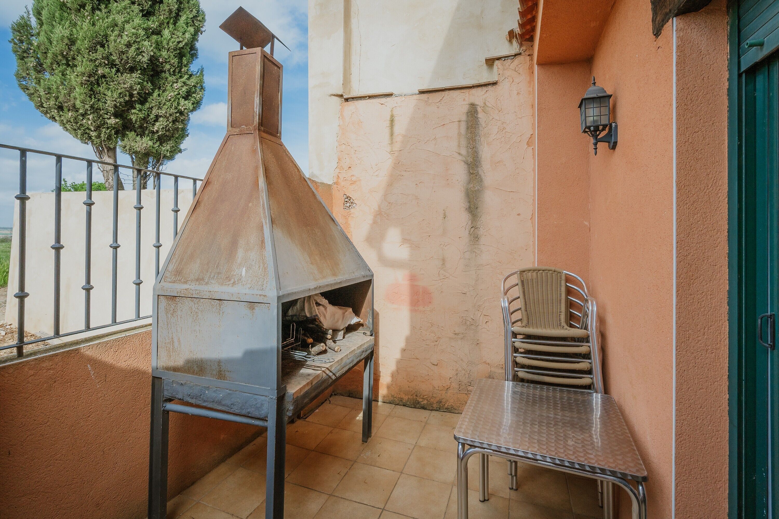 A patio with a metal grill, a table, chairs, and a tree.