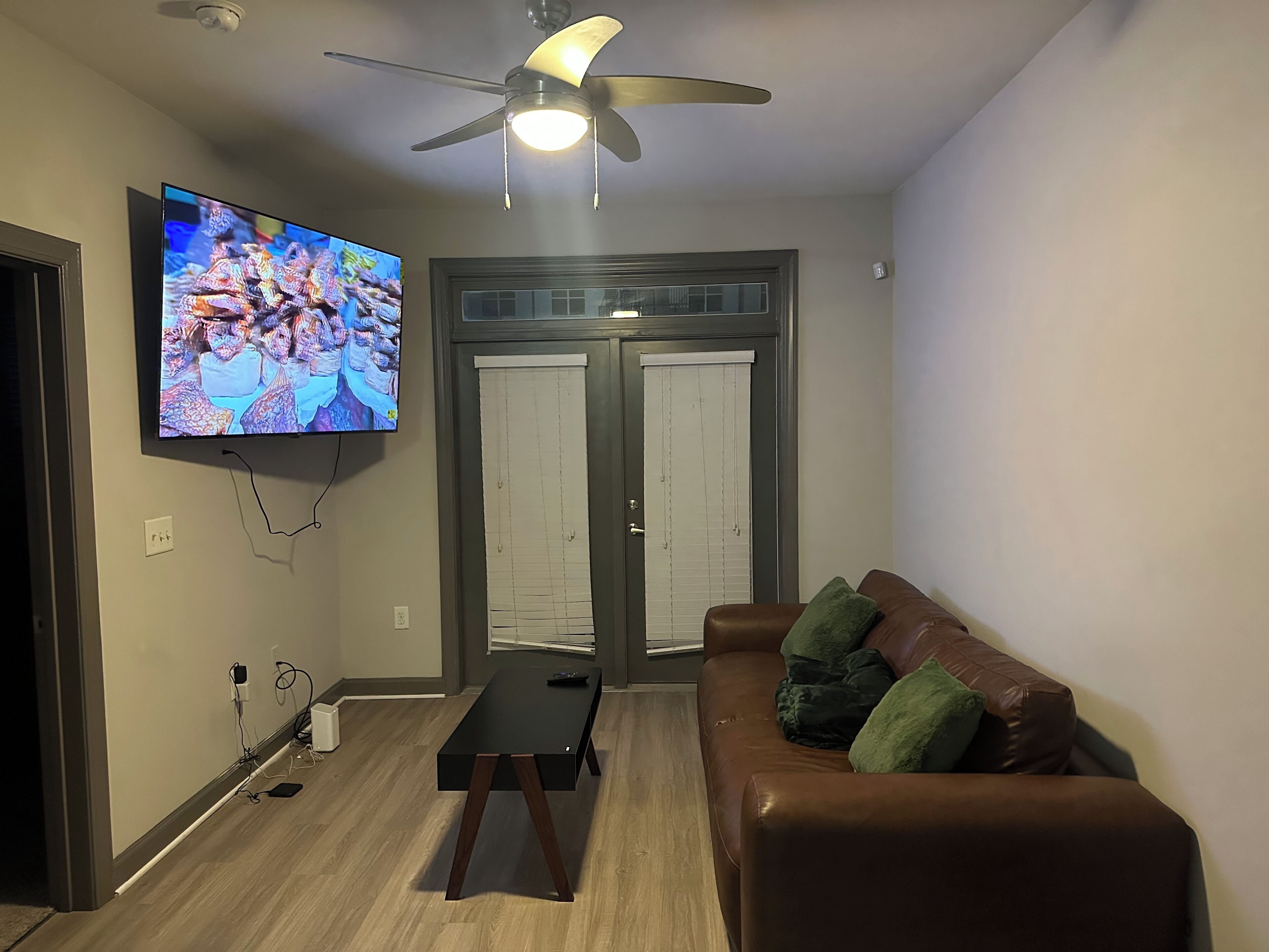 Ein Wohnzimmer mit Fernseher, Deckenventilator und einem braunen Ledersofa.