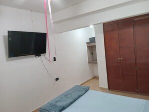 Un dormitorio con una cama, un televisor en la pared, un armario y una pequeña estantería.
