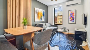 Ein modernes Wohnzimmer mit einer Wand aus Holzleisten, einem Esstisch mit Stühlen, einem Sofa, einem kleinen Couchtisch und einem Fernseher.