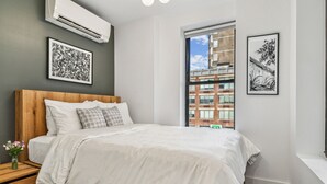 Ein modernes Schlafzimmer mit einem hölzernen Kopfteil, einem großen Bett, einem Nachttisch mit einer Vase sowie zwei gerahmten Kunstwerken an den Wänden.
