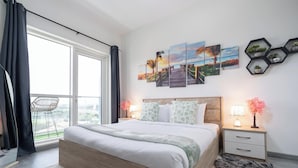 Ein modernes Schlafzimmer mit einem großen Bett, Blick auf die Stadt und einem Sonnenuntergangsbild an der Wand.
