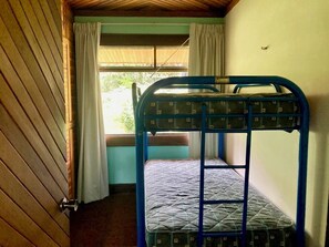 Une chambre avec un lit superposé, une fenêtre, des rideaux et une porte en bois.