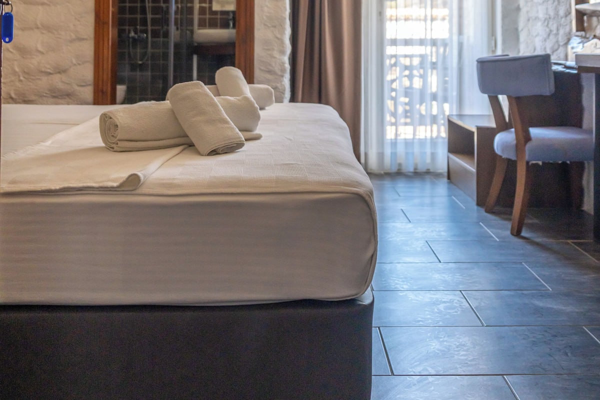 A hotel room with a bed, a desk, and a shower area.