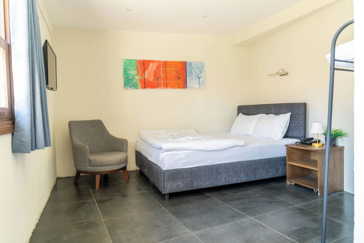 A bedroom with a bed, a chair, a nightstand, a lamp, and a painting on the wall.