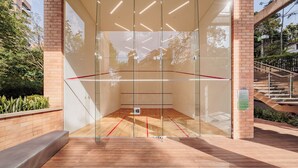 Un court de squash avec des murs en verre, un plancher en bois et un escalier à l’extérieur.