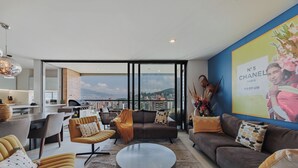 Un salon moderne avec un canapé, des fauteuils, une table basse et une vue sur le paysage urbain grâce à de grandes fenêtres.