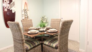 Un comedor con una mesa redonda, cuatro sillas de mimbre y un adorno en la pared.
