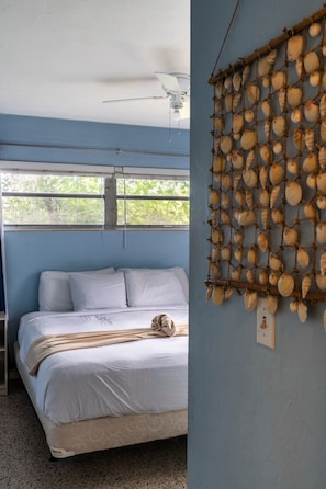 A bedroom with a bed, a ceiling fan, and a wall decoration of shells. - Private Coastal Haven: Fire Pit • Yard • Beach (Sarasota)