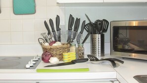 Una cocina con microondas, tabla de cortar, cesta de verduras y juego de cuchillos.
