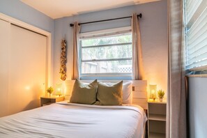 A bedroom with a bed, two bedside tables, a window with curtains, and a wall-mounted decoration. - Private Coastal Haven: Fire Pit • Yard • Beach (Sarasota)
