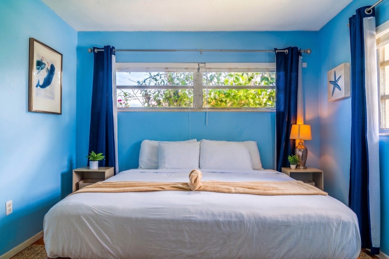 Une chambre à coucher avec un lit, une fenêtre avec des rideaux, une table de chevet avec une lampe et un mur décoré d’une étoile de mer.