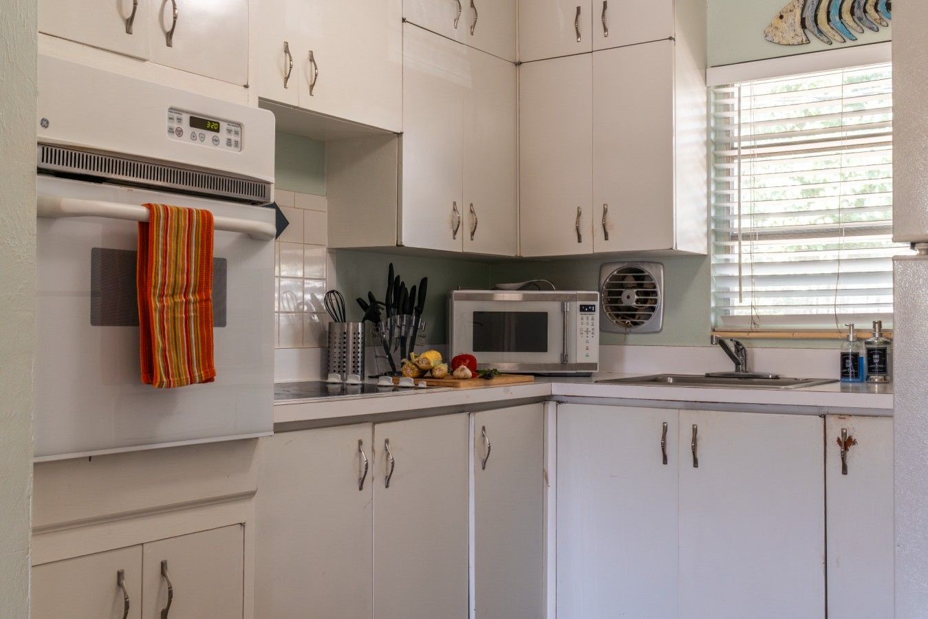 A kitchen with white cabinets, a microwave, a stove, and a window with blinds.