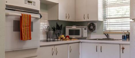 A kitchen with white cabinets, a microwave, a stove, and a window with blinds.