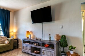 Ein Wohnzimmer mit flachbildfernseher an der Wand, einer Holztruhe für Unterhaltungselektronik mit Dekorationen, einer Couch und einer Lampe.