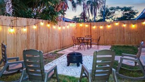 Un patio trasero con cerco de madera, luces colgantes y mobiliario exterior.