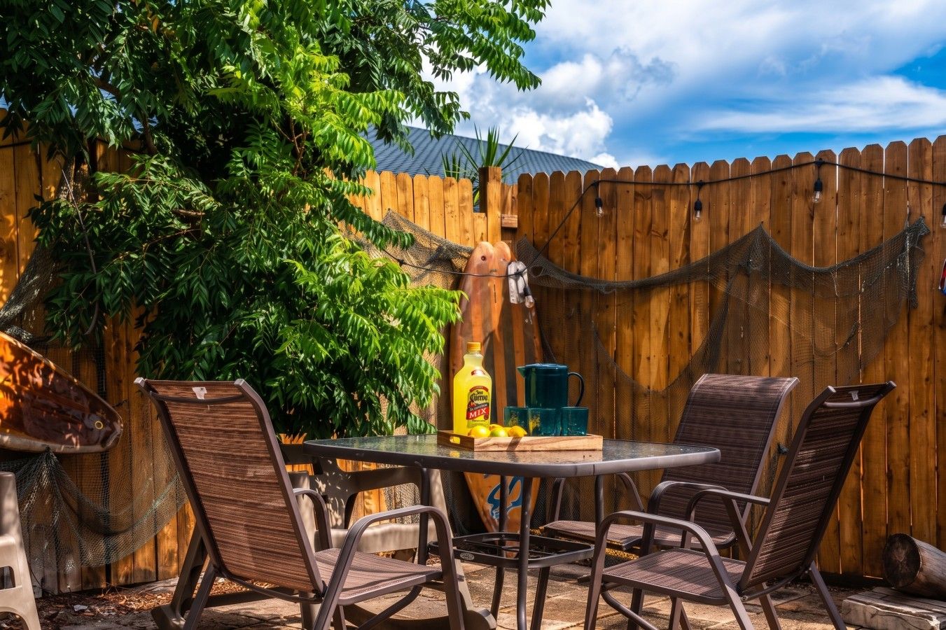 An outdoor patio with a table and chairs, surrounded by a wooden fence and greenery.