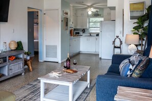 Ein modernes Wohnzimmer mit einem grauen Sofa, einem Couchtisch und einem Essbereich mit weißen Schränken und einem Deckenventilator.