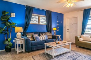 A living room with a blue wall, a sofa, a coffee table, and a door. - Private Coastal Haven: Fire Pit • Yard • Beach (Sarasota)