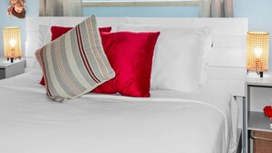 Una cama bien hecha con ropa de cama blanca y roja, dos lámparas de noche y una ventana con persianas.