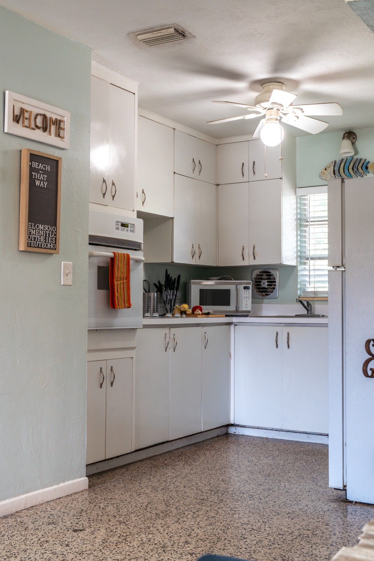 A kitchen with white cabinets, a ceiling fan, a microwave, and a sink.
