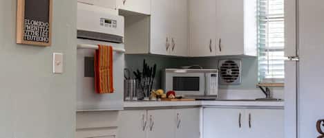 A kitchen with white cabinets, a ceiling fan, a microwave, and a sink.