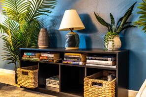 A bookshelf with books, a lamp, and decorative items against a blue wall. - Chic Local Hideaway: BBQ Nights • Near Beach (Sarasota)