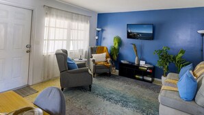 A living room with a sofa, armchair, coffee table, and a television on the wall. - Chic Local Hideaway: Yard |BBQ Nights | Near Beach (Sarasota)