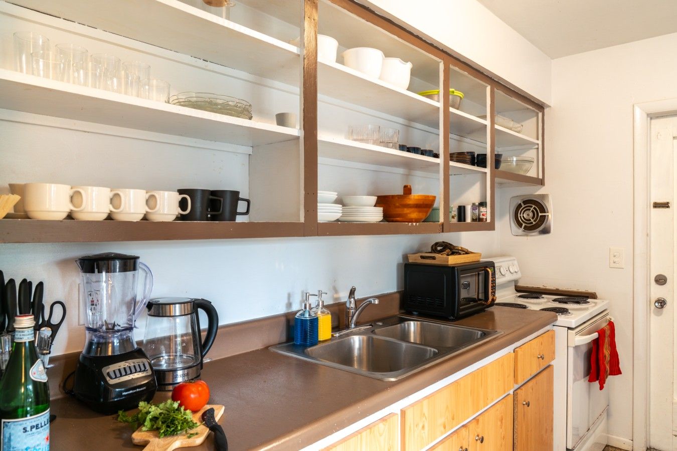 A kitchen with a built-in microwave, toaster, and stove. There are shelves above the counter holding dishes and cups.