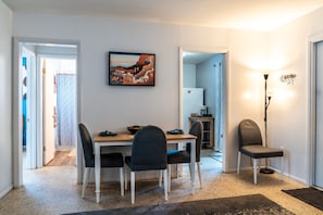 A dining area with a table and chairs, a painting on the wall, and a kitchen in the background. - Chic Local Hideaway: BBQ Nights • Near Beach (Sarasota)