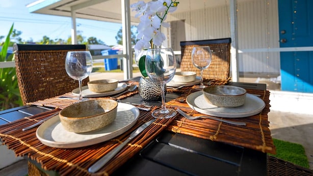 An outdoor dining setup with wicker chairs, a table, and a decorative orchid centerpiece. - Chic Local Hideaway: Yard |BBQ Nights | Near Beach (Sarasota)