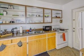 Een keuken met houten kastjes, een magnetron, een fornuis en diverse keukengerei.