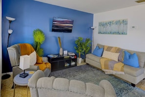 Een woonkamer met een blauwe muur, een bank, een fauteuil, een salontafel en een televisie.