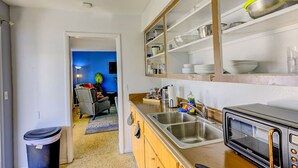 A compact kitchen with a microwave, sink, and shelves above. - Chic Local Hideaway: Yard |BBQ Nights | Near Beach (Sarasota)