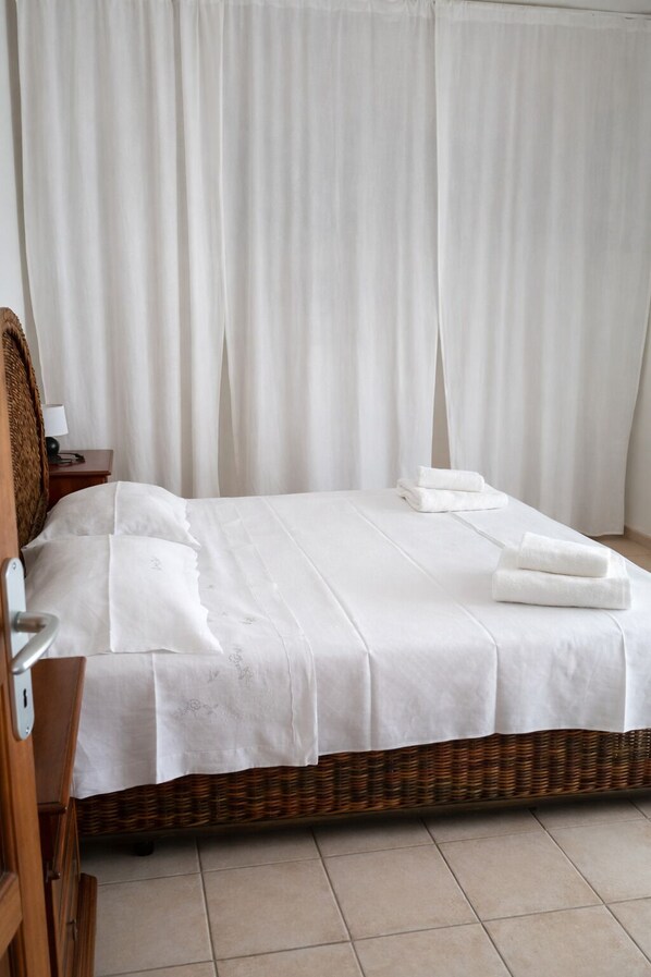 Una habitación de hotel con una cama, una mesita de noche, una lámpara y una silla de mimbre.