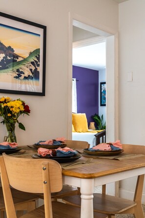 Ein Essbereich mit einem Holztisch, gedeckt für zwei Personen, einer Blumenvase und einem gerahmten Bild an der Wand.
