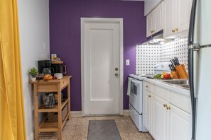 A compact kitchen with a white door, purple walls, and a small countertop with kitchen utensils. - Chic Sarasota Gem: Beach • BBQ • Workspace • Patio (Sarasota)