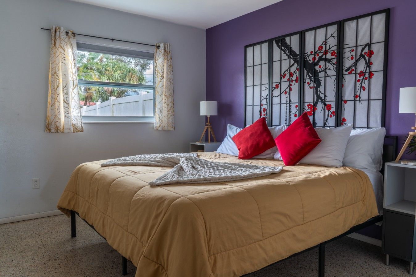 Un dormitorio con cama, dos mesitas de noche, una ventana con cortinas y una obra de arte en la pared.