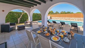 An outdoor dining area with a pool view, covered seating, and breakfast setup. - Villa Maype by 3 Villas Menorca (Cap d`Artrutx)