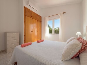 Une chambre à coucher avec un lit, une armoire, une fenêtre avec des rideaux et une lampe.