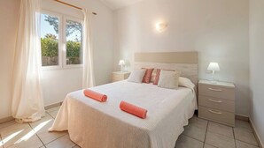 A bedroom with a bed, nightstands, a window with curtains, and a wall-mounted light. - Villa Maype by 3 Villas Menorca (Cap d`Artrutx)