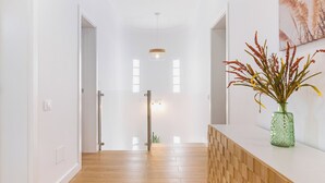 Un pasillo con suelo de madera, paredes blancas, una puerta de cristal y un jarrón verde con plantas.