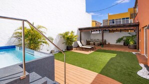 Un patio trasero con piscina, césped artificial y un área de estar techada.